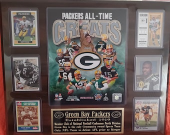 May include: A framed display of Green Bay Packers memorabilia. It includes player cards and a central graphic with the words "Packers All-Time Greats." The display features the team logo and text about the team's history.