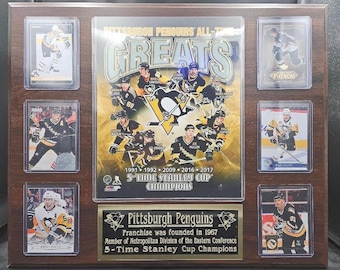 Puede incluir: Una placa de madera con recuerdos de los Pittsburgh Penguins. La placa incluye tarjetas de hockey, un gráfico central con los jugadores del equipo y el texto "Pittsburgh Penguins All-Time Greats" y "5-Time Stanley Cup Champions."