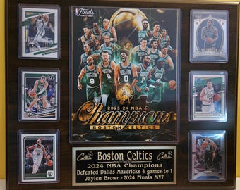 May include: A framed Boston Celtics commemorative display. It features a central image of the team, surrounded by basketball cards. The display includes text that reads "2024 NBA Champions" and "Jaylen Brown-2024 Finals MVP."