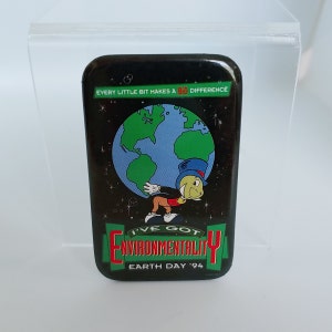 May include: A black and green button with a cartoon character holding a globe. The text on the button reads "Every little bit makes a big difference. I've got environmentality. Earth Day '94."