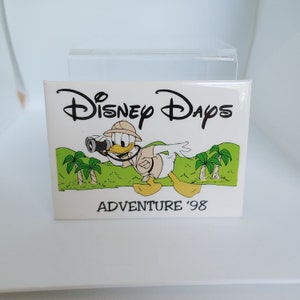 May include: A white sticker with a cartoon image of Donald Duck dressed as an explorer holding binoculars. The text "Disney Days Adventure '98" is printed below the image.