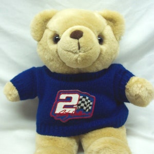May include: A tan plush teddy bear wearing a blue sweater with a white and black checkered flag and the number "2" on the front. The sweater also has the name "Jeff Gordon" written on it.