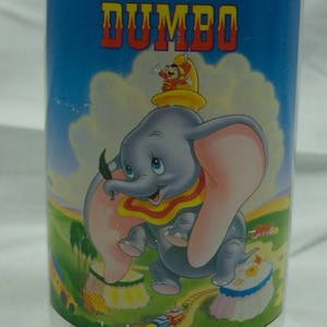 May include: A clear plastic glass with a blue background and a picture of Dumbo the elephant from the Disney movie Dumbo. The text "A Walt Disney Classic DUMBO" is printed on the glass.