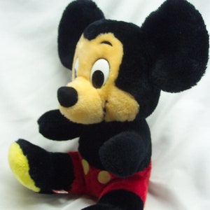 May include: A plush Mickey Mouse toy with black ears, a black nose, and yellow shoes. The toy is wearing red shorts with white polka dots.