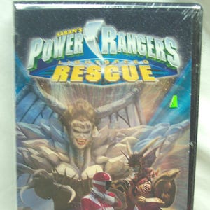 Puede incluir: Una cinta VHS de Power Rangers Lightspeed Rescue. La portada presenta un Power Ranger rojo, villanos y el texto "The Queen's Wrath". El título es azul y amarillo.