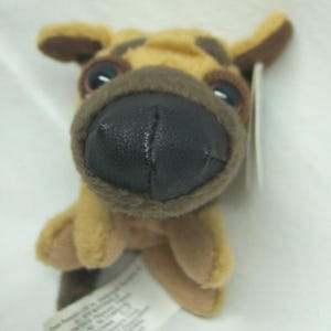 May include: A plush toy dog with a tan and brown color scheme. The dog has a large black nose, brown ears, and red eyes. A white tag is attached to the toy.