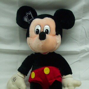 May include: A plush black Mickey Mouse toy with yellow shoes and red shorts with yellow buttons. The toy has a white tag on its ear that says "Applause".