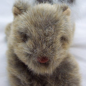 May include: A plush gray and brown squirrel toy with a fluffy tail. The squirrel has a pink nose and is lying on its belly with its paws tucked under its chest.