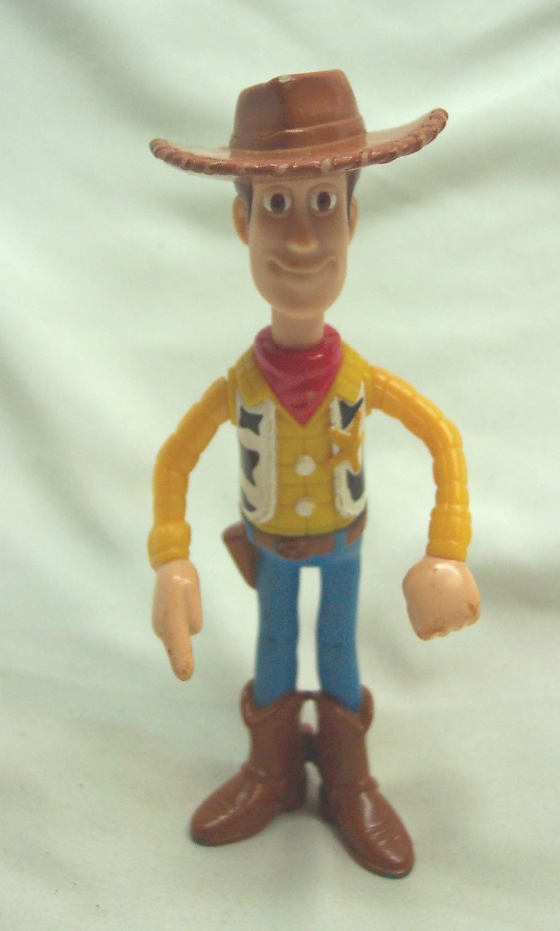 Pu&ograve; includere: Una figurina di plastica di Woody del franchise Toy Story. Woody indossa un cappello da cowboy marrone, una camicia gialla con una bandana rossa, una cintura marrone, jeans blu e stivali marroni. Ha una stella da sceriffo sul suo gilet.