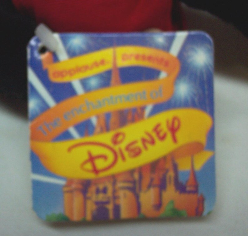 May include: A blue and yellow tag with the text "The enchantment of Disney" and a picture of Cinderella's castle.