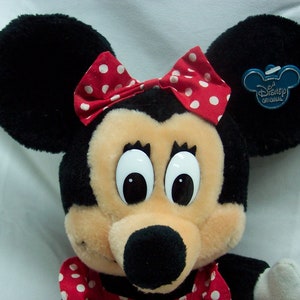 May include: A plush Minnie Mouse toy with large eyes, a black nose, and a red bow with white polka dots. The toy has a blue tag that says "Disney Original".