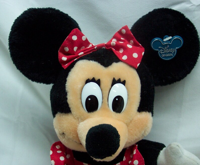 May include: A plush Minnie Mouse toy with large eyes, a black nose, and a red bow with white polka dots. The toy has a blue tag that says "Disney Original".