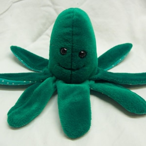 May include: A plush green octopus toy with eight tentacles. The octopus has a smiling face with two black eyes. The tips of the tentacles have white polka dots. The toy is made of soft, velvety material.