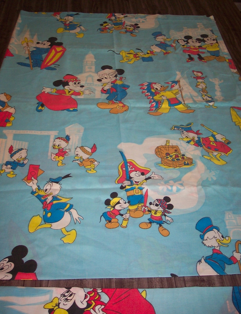 Puede incluir: Una tela azul y blanca con un patr&oacute;n repetido de personajes de Mickey Mouse y Donald Duck. Los personajes est&aacute;n vestidos con varios disfraces, incluyendo un pirata, un vaquero y un chef. La tela es perfecta para la habitaci&oacute;n de un ni&ntilde;o o una sala de juegos.