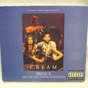 May include: A compact disc maxi-single featuring the album "Cream" by Prince and The New Power Generation. The cover has a blue background with a central image of Prince and other band members. The text "Cream" and "Prince and The New Power Generation" are visible.