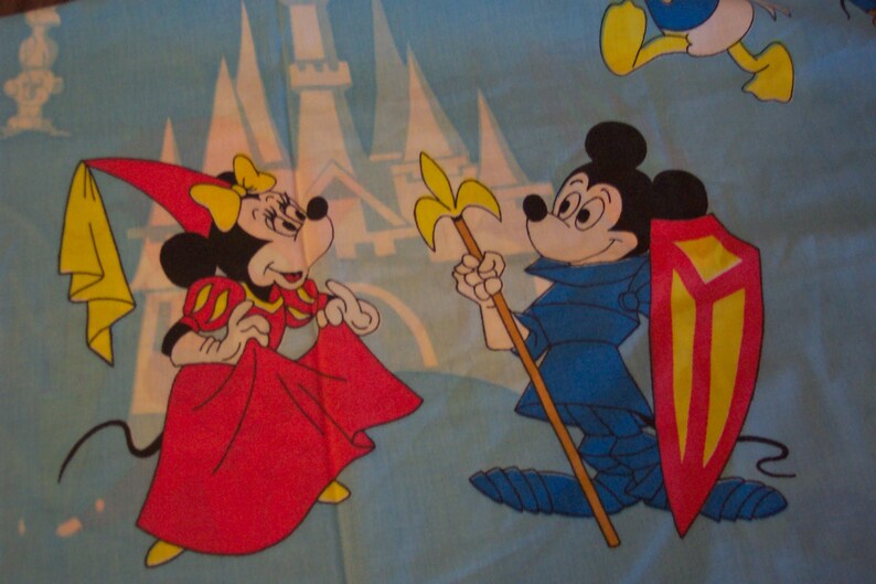 Puede incluir: Un personaje de dibujos animados rojo y amarillo con un escudo y una lanza se encuentra junto a un personaje de dibujos animados rojo y amarillo que lleva un vestido rojo y una capa amarilla. Los personajes est&aacute;n frente a un castillo azul y blanco.