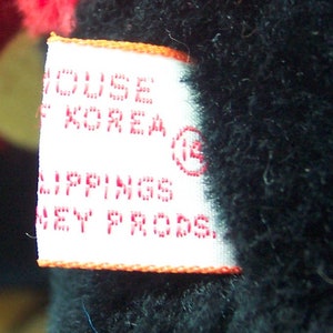 May include: White tag with red text that reads "HOUSE OF KOREA" and "LIPPINGS DISNEY PRODS." with a red circle containing the number "13" in the upper right corner.