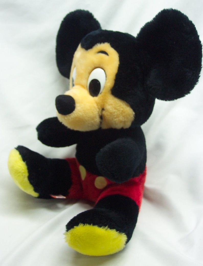 May include: A plush Mickey Mouse toy with black ears, a black nose, and yellow shoes. The toy is wearing red shorts with white polka dots.