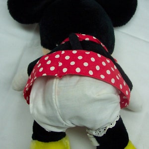 May include: A black and white plush toy of a cartoon mouse wearing a red and white polka dot dress. The toy has yellow feet and is sitting on a white surface.