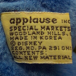 Puede incluir: Etiqueta amarilla con texto negro que dice "applause inc. Special Markets Woodland Hills, CA Hecho en Corea &copy; Disney Reg. No. PA 291 CHI Contenido: Todo material nuevo"