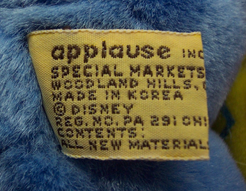Puede incluir: Etiqueta amarilla con texto negro que dice "applause inc. Special Markets Woodland Hills, CA Hecho en Corea &copy; Disney Reg. No. PA 291 CHI Contenido: Todo material nuevo"