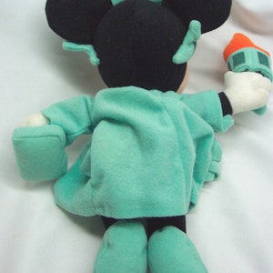 Peut inclure: Une peluche de Mickey Mouse habill&eacute;e en statue de la Libert&eacute;. La peluche porte une robe verte avec une couronne et tient un flambeau miniature.
