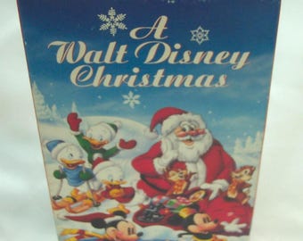 May include: A Walt Disney Christmas VHS tape with a red top edge and blue cover. The cover features Santa Claus, Mickey Mouse, Minnie Mouse, and Donald Duck in a snowy scene. Text includes A Walt Disney Christmas, Stock No. 092, 46 Minutes/Color.