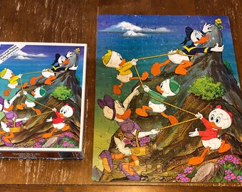 May include: A vintage Donald Duck jigsaw puzzle with 100 large pieces. The puzzle depicts Donald Duck and his nephews climbing a mountain with ropes. The puzzle box features a colorful image of the ducks climbing the mountain. The box also includes the text "100 Large Pieces, Fun for Everyone!"