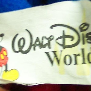 May include: White tag with black text reading "Walt Disney World." A cartoon image of Mickey Mouse in red shorts is on the left side of the tag.