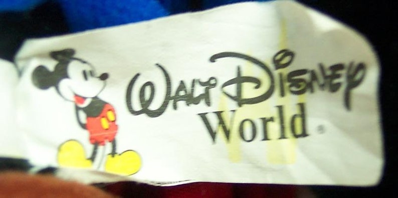May include: White tag with black text reading "Walt Disney World." A cartoon image of Mickey Mouse in red shorts is on the left side of the tag.