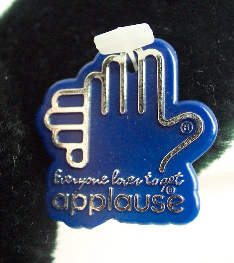 May include: Blue plastic tag with a silver hand outline and the text "Everyone loves to get applause" in silver lettering.