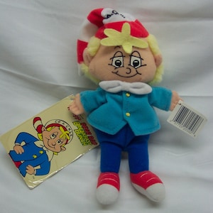 May include: A plush toy of a boy wearing a red and white hat, blue jacket, blue pants, and red shoes. The toy is holding a tag that says "General Mills Breakfast Bunch Crackle"