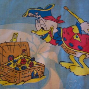 Puede incluir: Un pato pirata de dibujos animados con un traje rojo y azul sostiene un telescopio y se encuentra junto a un cofre del tesoro de madera lleno de joyas.