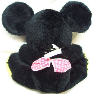 May include: Black plush toy mouse with large ears and a pink polka dot bow. The toy is sitting on a white surface.