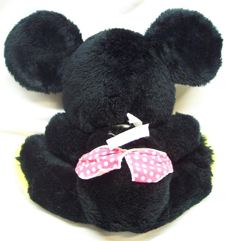 May include: Black plush toy mouse with large ears and a pink polka dot bow. The toy is sitting on a white surface.