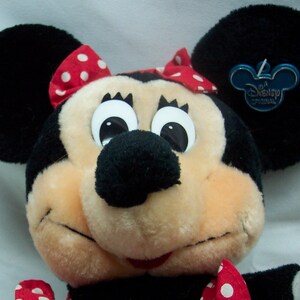 May include: A plush Minnie Mouse toy with a red and white polka dot bow, large black eyes, and a black nose. The toy has a Disney Original tag attached to one ear.