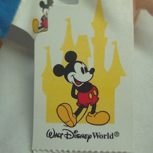 May include: A white tag featuring Mickey Mouse in his classic outfit, with a yellow castle silhouette in the background. The tag reads "Walt Disney World". A smaller Mickey Mouse image is visible on the upper left corner.