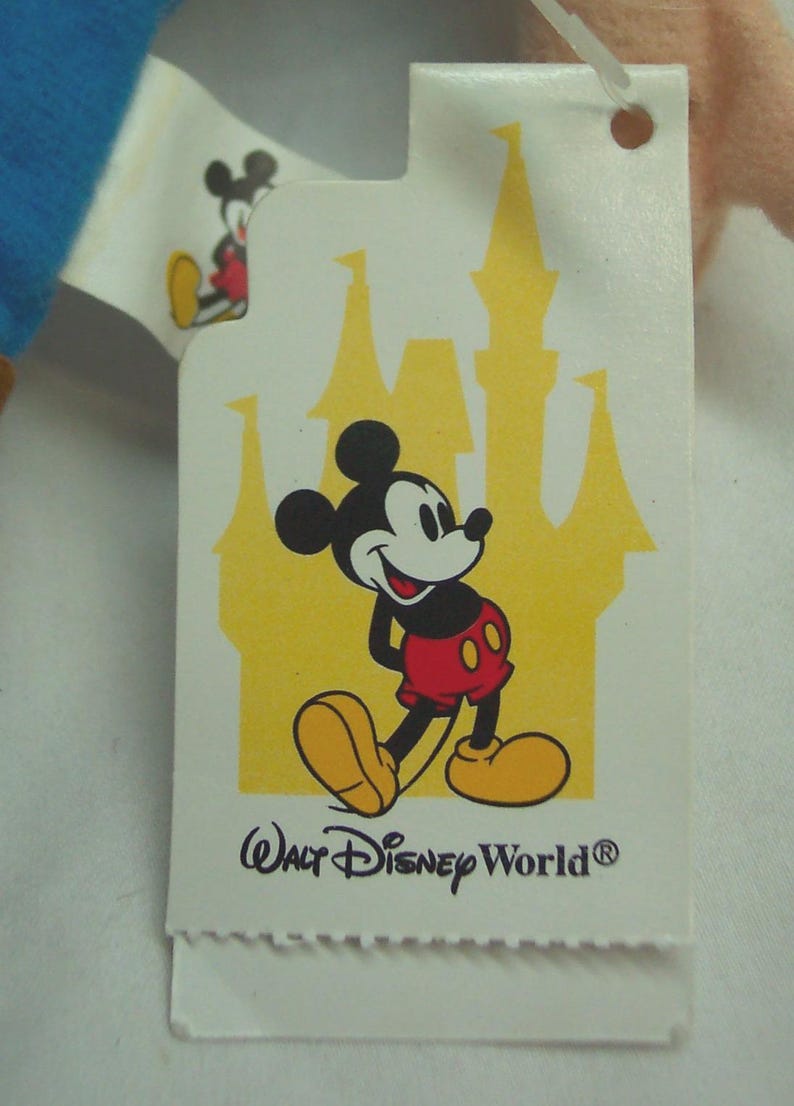 May include: A white tag featuring Mickey Mouse in his classic outfit, with a yellow castle silhouette in the background. The tag reads "Walt Disney World". A smaller Mickey Mouse image is visible on the upper left corner.