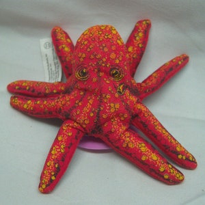 May include: Red and yellow plush octopus with black eyes. The octopus has eight tentacles and is made of a soft, textured fabric.