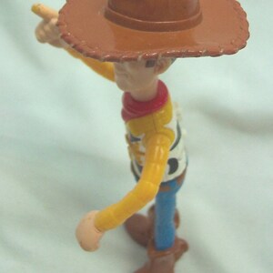 Pu&ograve; includere: Una figurina di plastica di Woody del franchise Toy Story. Woody indossa il suo cappello da cowboy marrone distintivo, una camicia gialla a maniche lunghe, un bandana rosso, jeans blu e stivali marroni. Sta tenendo il braccio destro teso, puntando con l'indice.
