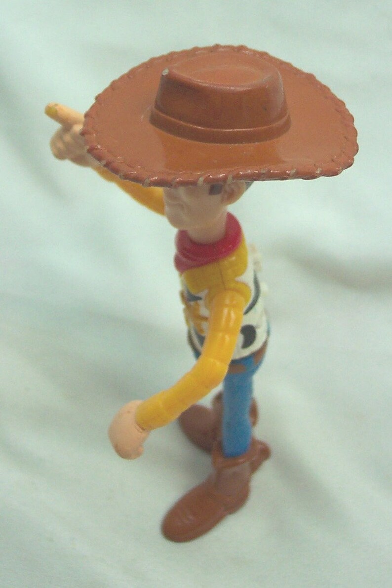 Pu&ograve; includere: Una figurina di plastica di Woody del franchise Toy Story. Woody indossa il suo cappello da cowboy marrone distintivo, una camicia gialla a maniche lunghe, un bandana rosso, jeans blu e stivali marroni. Sta tenendo il braccio destro teso, puntando con l'indice.
