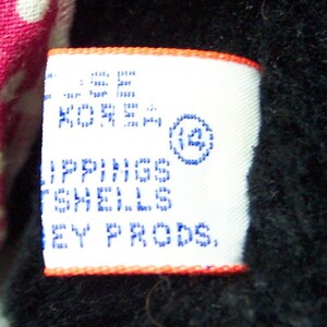 May include: White tag with blue text that reads "Lippings Shells Ney Prods." and a blue circle with the number "12" inside. The tag has an orange border.