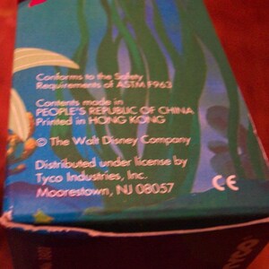 May include: A blue and green box with a cartoon image of a mermaid. The box has text that reads "Conforms to the Safety Requirements of ASTM F963", "Contents made in PEOPLE'S REPUBLIC OF CHINA", "Printed in HONG KONG", "The Walt Disney Company", "Distributed under license by Tyco Industries, Inc.", "Moorestown, NJ 08057", and "CE".