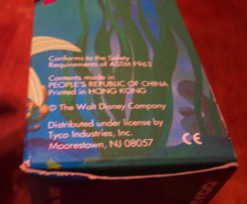 May include: A blue and green box with a cartoon image of a mermaid. The box has text that reads "Conforms to the Safety Requirements of ASTM F963", "Contents made in PEOPLE'S REPUBLIC OF CHINA", "Printed in HONG KONG", "The Walt Disney Company", "Distributed under license by Tyco Industries, Inc.", "Moorestown, NJ 08057", and "CE".