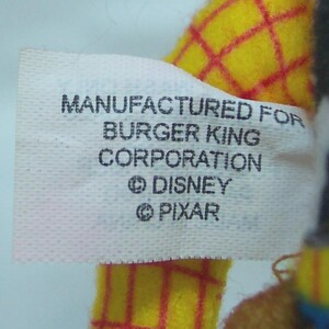Puede incluir: Primer plano de una etiqueta blanca con texto negro que dice "MANUFACTURED FOR BURGER KING CORPORATION &copy; DISNEY &copy; PIXAR". La etiqueta est&aacute; adherida a un juguete de peluche amarillo con l&iacute;neas de cuadr&iacute;cula rojas.