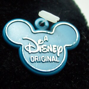 May include: A blue plastic Disney tag with Mickey Mouse ears, featuring the text "A Disney Original".