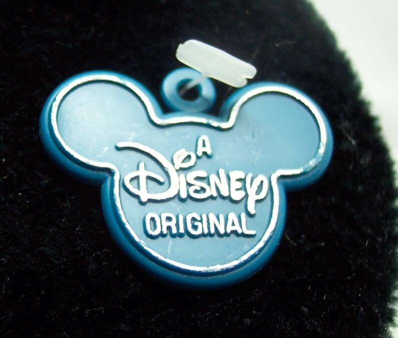 May include: A blue plastic Disney tag with Mickey Mouse ears, featuring the text "A Disney Original".