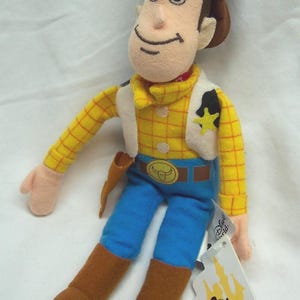 May include: A plush Woody doll from Disney's Toy Story. The doll is wearing a brown cowboy hat, yellow plaid shirt, blue pants, and brown boots. It has a white vest, a sheriff's badge, and a belt buckle. A Disney World tag is attached.