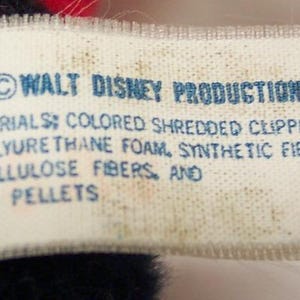 May include: A close-up of a white tag with blue text. The tag reads "RIGHT &copy; WALT DISNEY PRODUCTIONS MATERIALS: COLORED SHREDDED CLIPPINGS ED POLYURETHANE FOAM, SYNTHETIC FIBERS ED CELLULOSE FIBERS, AND LENE PELLETS."