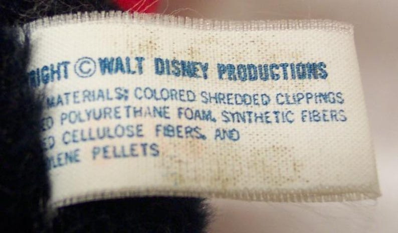May include: A close-up of a white tag with blue text. The tag reads "RIGHT &copy; WALT DISNEY PRODUCTIONS MATERIALS: COLORED SHREDDED CLIPPINGS ED POLYURETHANE FOAM, SYNTHETIC FIBERS ED CELLULOSE FIBERS, AND LENE PELLETS."